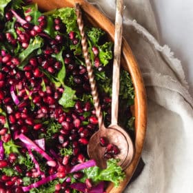 a wooden bowl of pomegranate kale salad with two serving spoons