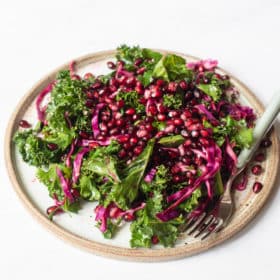 a serving of pomegranate kale salad on a plate next to a fork