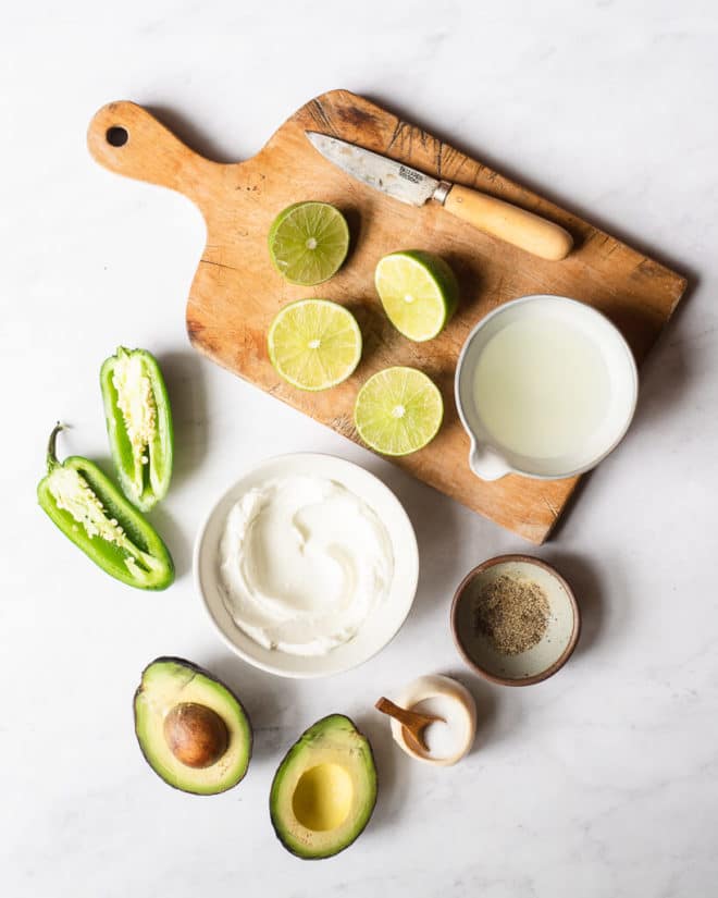 all of the ingredients for an avocado dressing in bowls and on a cutting board on a marble surface