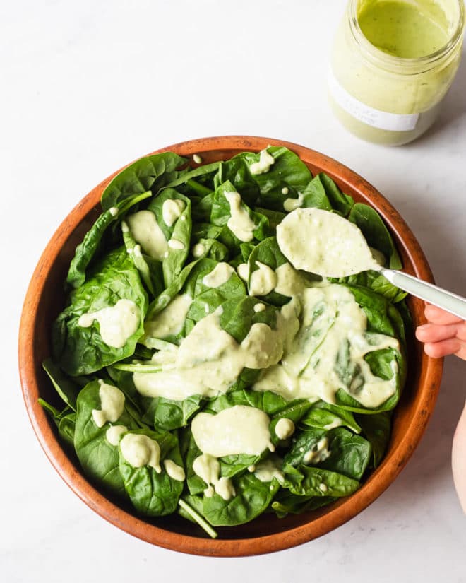 a wooden bowl of spinach leaves drizzled with avocado dressing