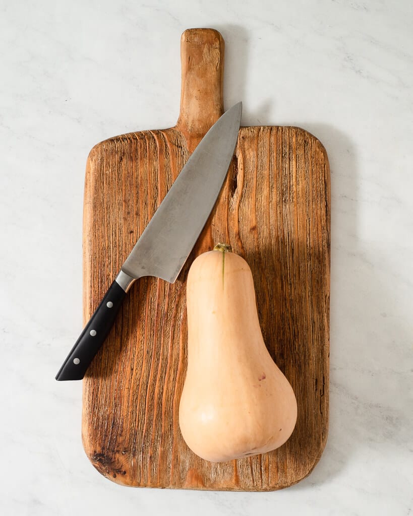 a butternut squash on a wooden cutting board next to a large knife