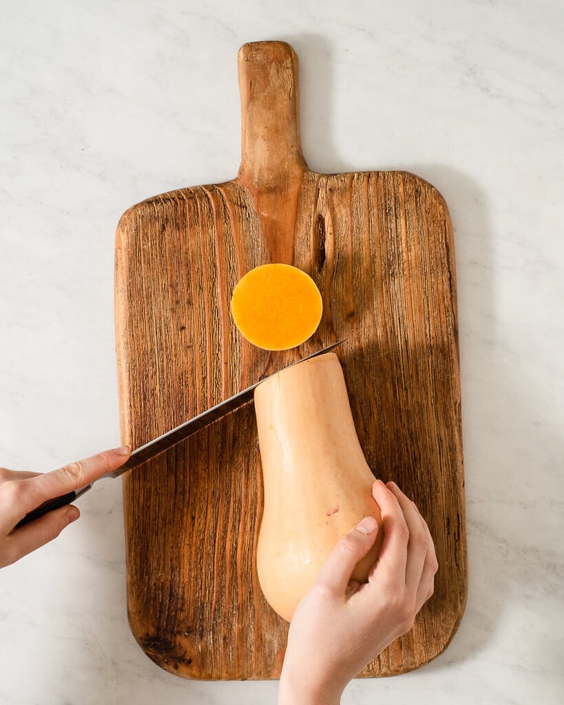 a person cutting the top off of a butternut squash on a wooden cutting board
