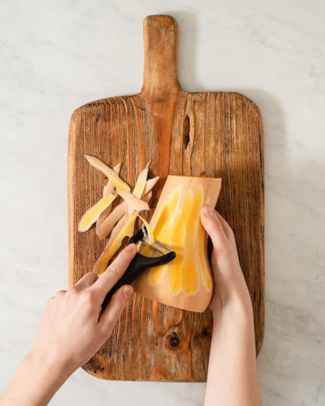 a person peeling a butternut squash on a wooden cutting board