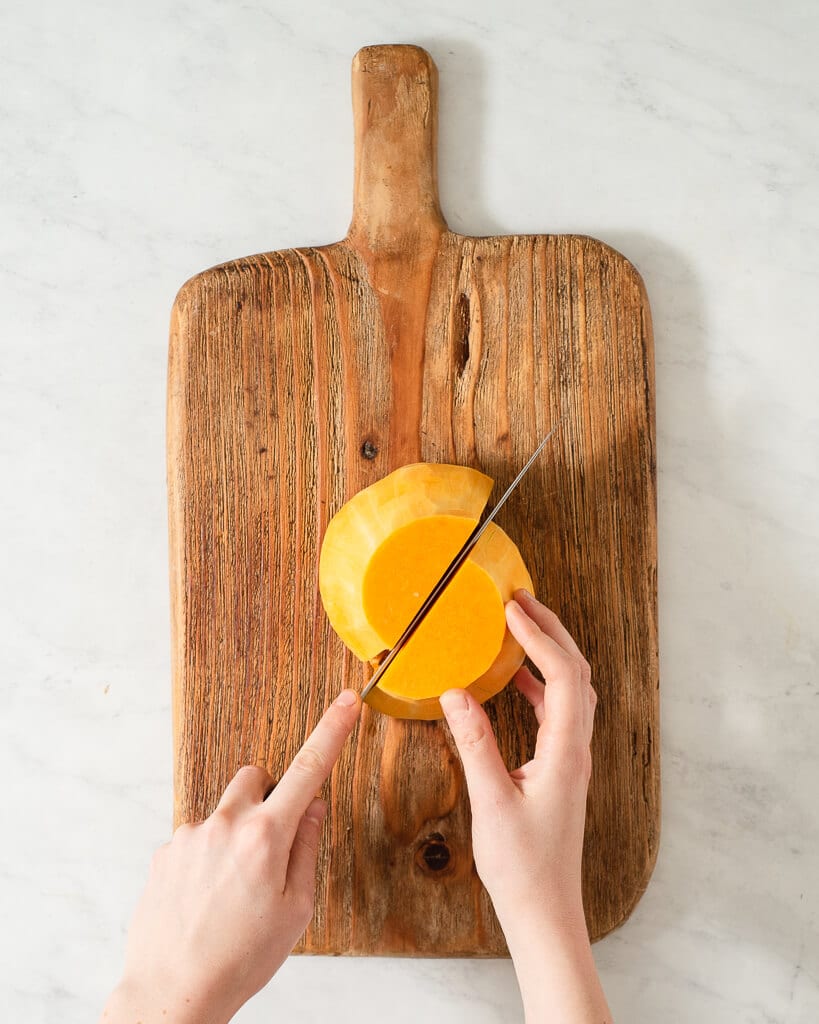 a person cutting a butternut squash in half on a wooden cutting board using a large knife