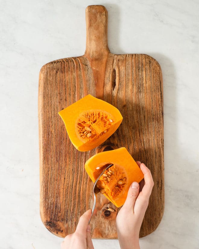 a person scooping the insides out of a butternut squash