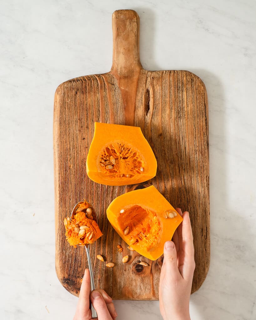 a person scooping the insides out of a butternut squash