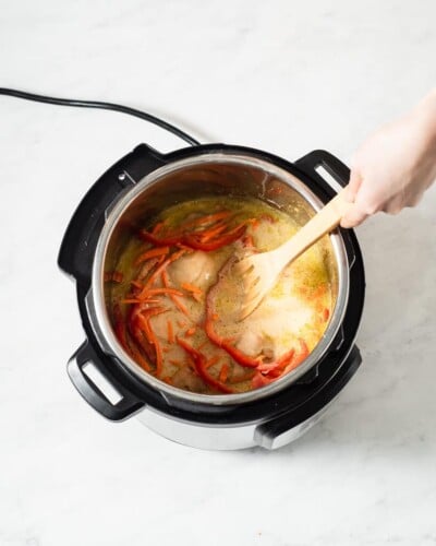 a person stirring together instant pot green curry chicken using a wooden spoon