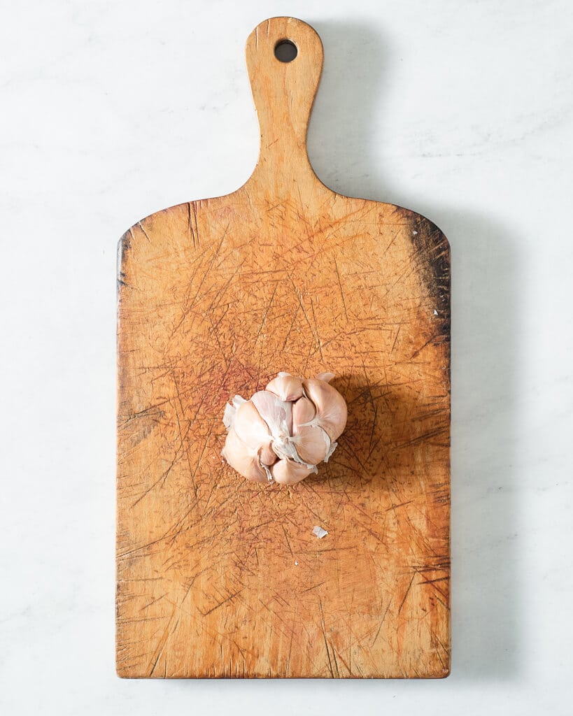 a large bulb of garlic sitting on a wooden cutting board