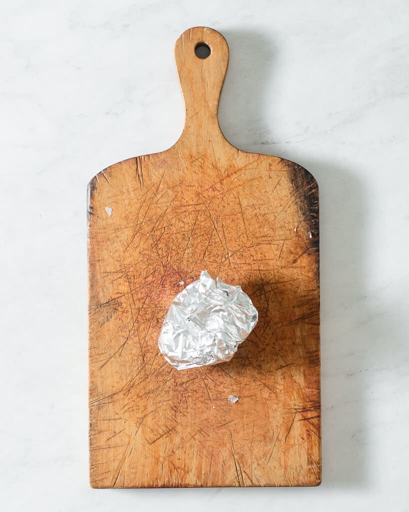 a bulb of roasted garlic wrapped in foil sitting on a wooden cutting board