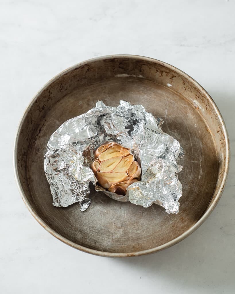 a bulb of roasted garlic wrapped in foil sitting in a circular baking dish