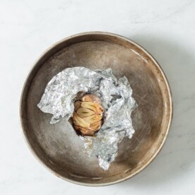a bulb of roasted garlic wrapped in foil sitting in a circular baking dish