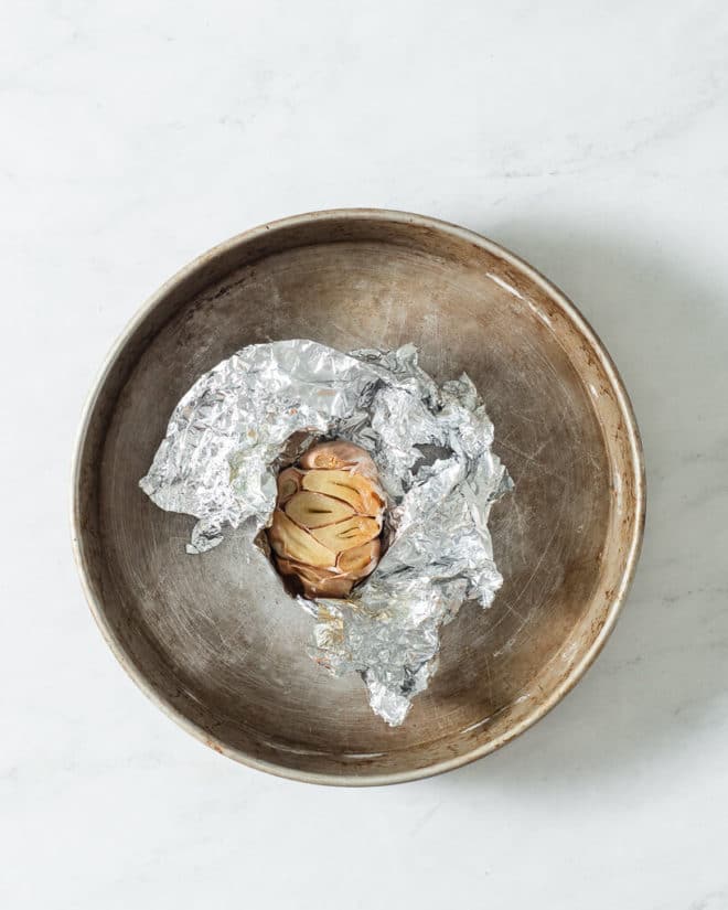 a bulb of roasted garlic wrapped in foil sitting in a circular baking dish