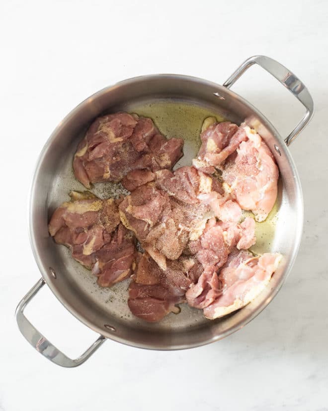 a person searing chicken thighs in a large stainless steel pot