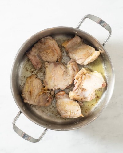 a person searing chicken thighs in a large stainless steel pot