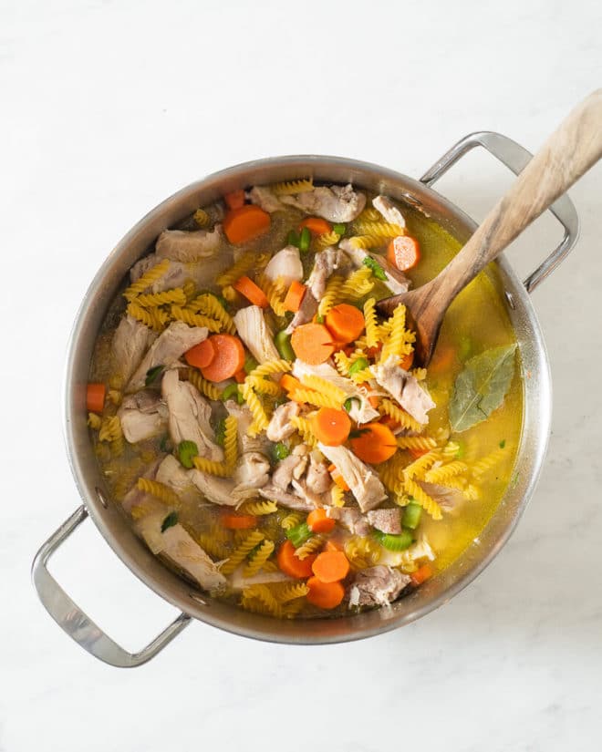 a large stainless steel pot of chicken noodle soup with a wooden spoon sticking out of it