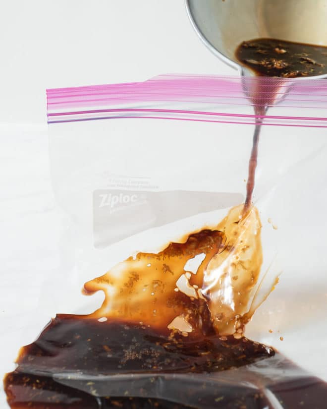 a person pouring a grilled chicken marinade into a large ziplock bag