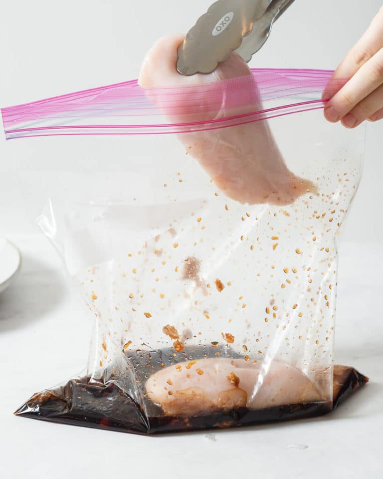 a person adding raw chicken breasts into a large ziplock bag of grilled chicken marinade
