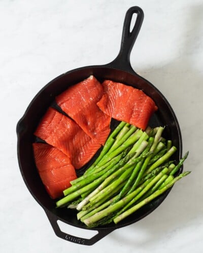 4 filets of salmon searing next to asparagus in a cast iron skillet