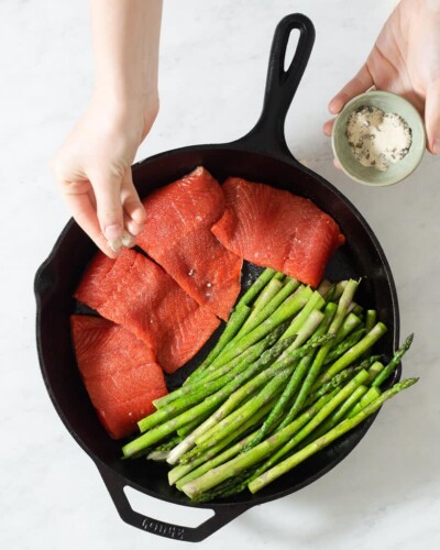 4 filets of salmon searing next to asparagus in a cast iron skillet