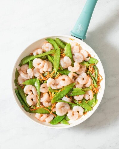 snow peas, carrots, onions, and shrimp sauteing in a pan