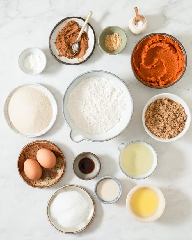 all of the ingredients for classic pumpkin bread in different sized bowls on a marble surface