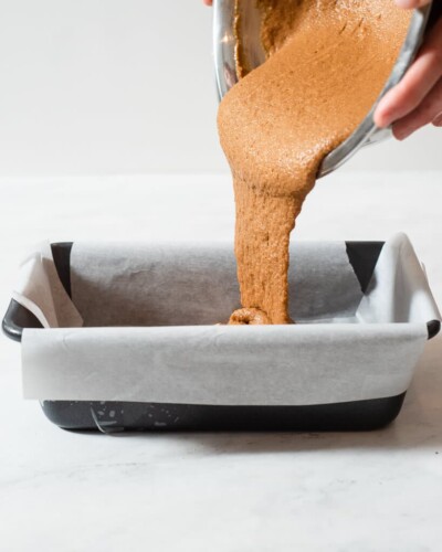 a person pouring in healthy pumpkin bread batter into a loaf pan