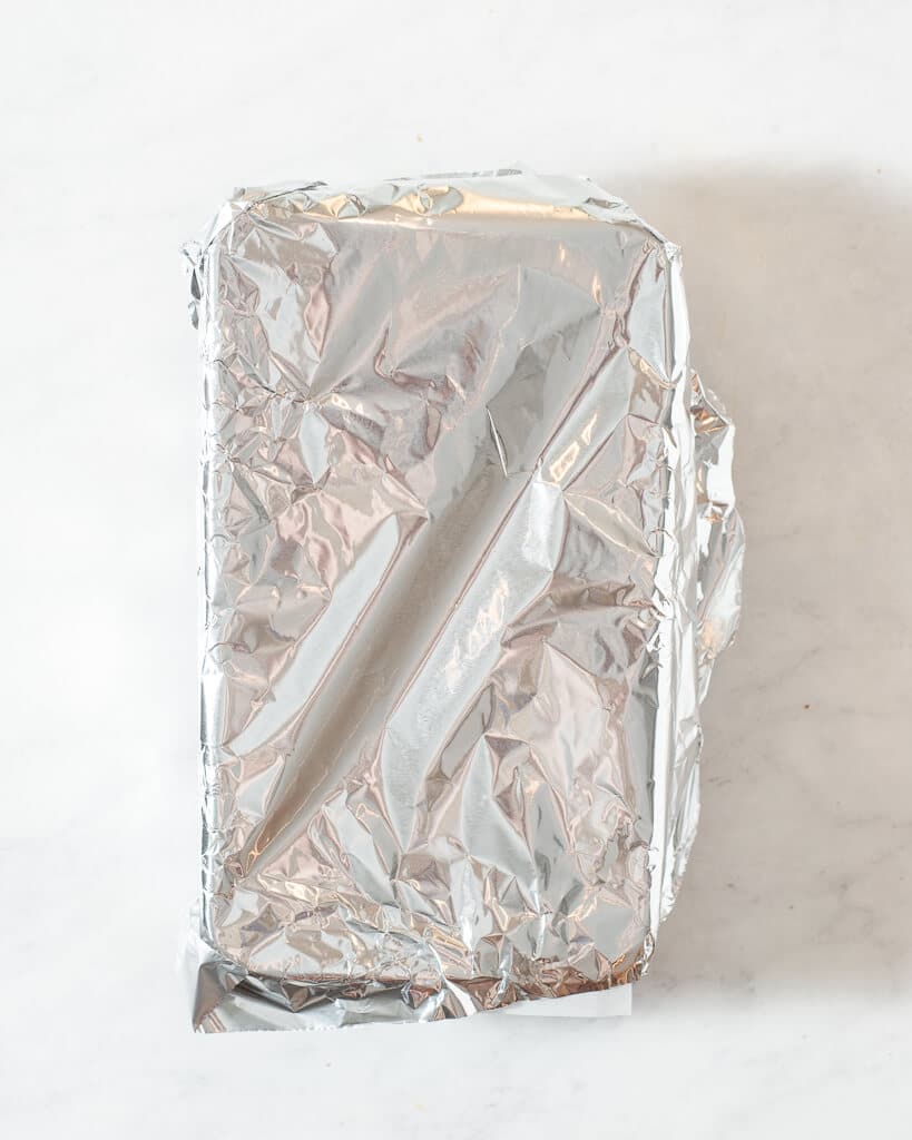 a loaf of healthy pumpkin bread in a parchment lined loaf pan covered with foil