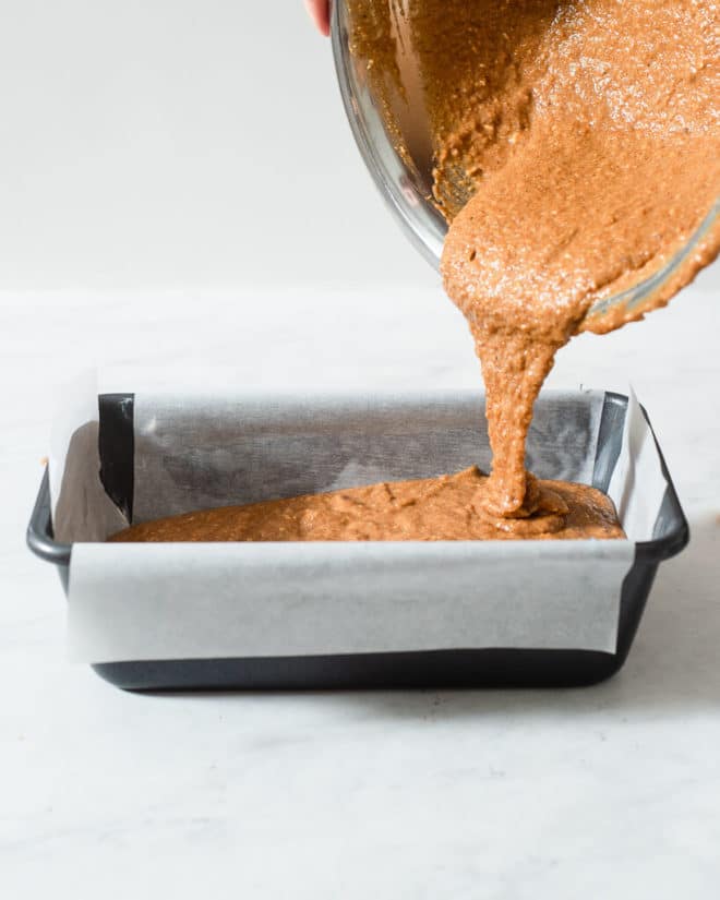 a person pouring keto pumpkin bread batter into a loaf pan