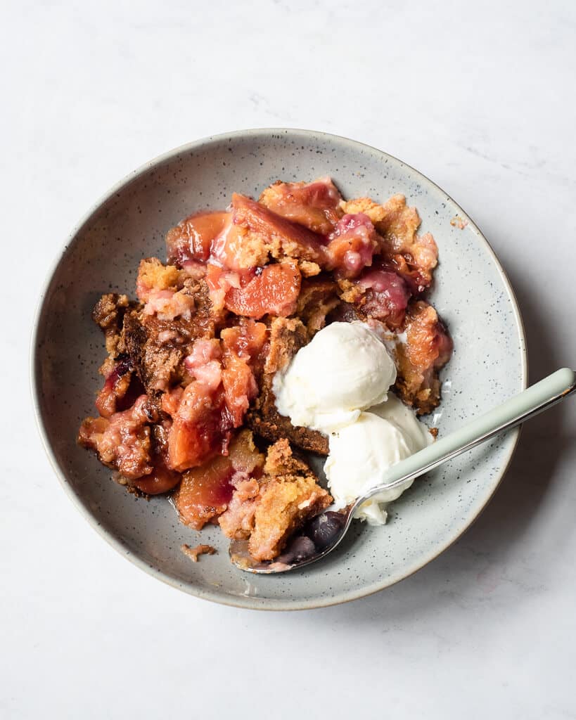 a serving of peach dump cake with two small scoops of vanilla ice cream
