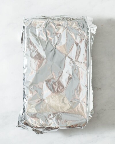 a loaf pan of baked vegan pumpkin bread covered with foil