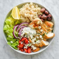 a green chicken power bowl made with brown rice, chicken, olives, cherry tomatoes, hummus, and lettuce