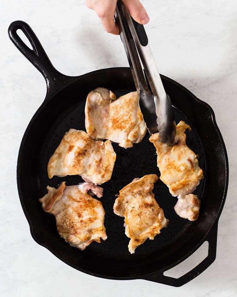 chicken thighs pan searing in a cast iron skillet