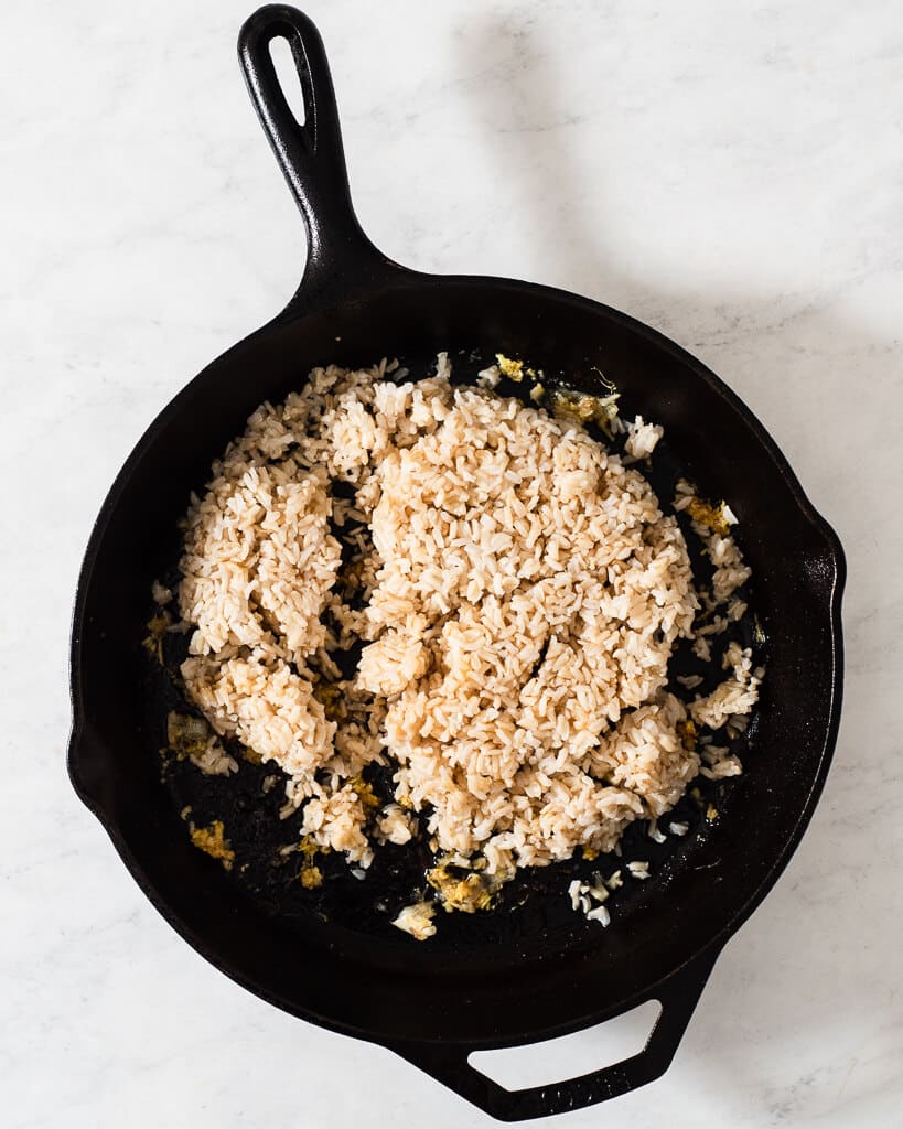 rice added to a cast iron skillet with ginger and garlic to start a fried rice dish