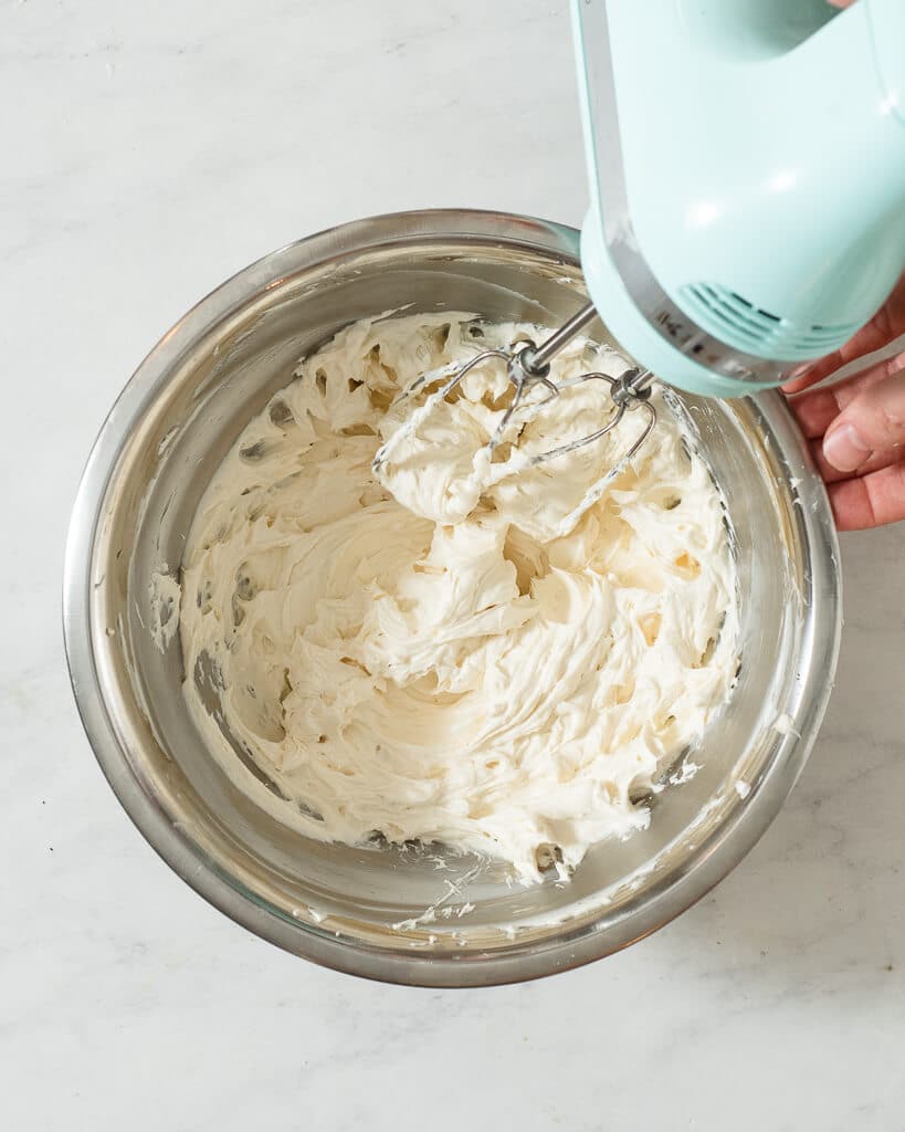 a person beating together the ingredients for cream cheese frosting