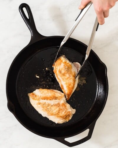 a person searing chicken breasts in a cast iron skillet