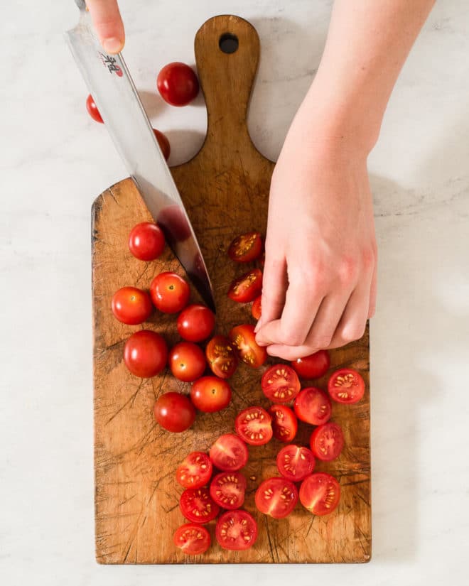 a person halving cherry tomatoes on a wooden cutting board