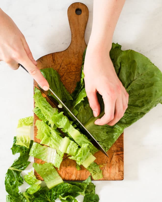 a person chopping romaine lettuce on a wooden cutting board
