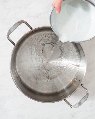 a person adding all of the ingredients for a pork chop brine into a large stainless steel pot