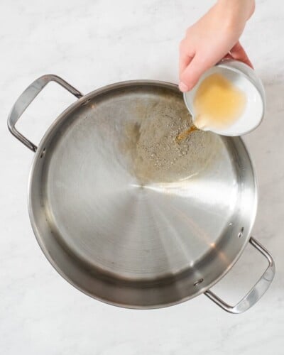 a person adding all of the ingredients for a pork chop brine into a large stainless steel pot