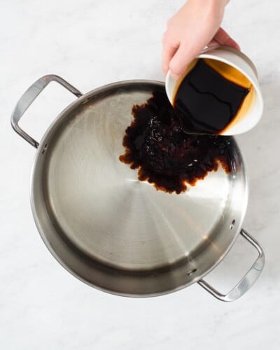 a person adding all of the ingredients for a pork chop brine into a large stainless steel pot