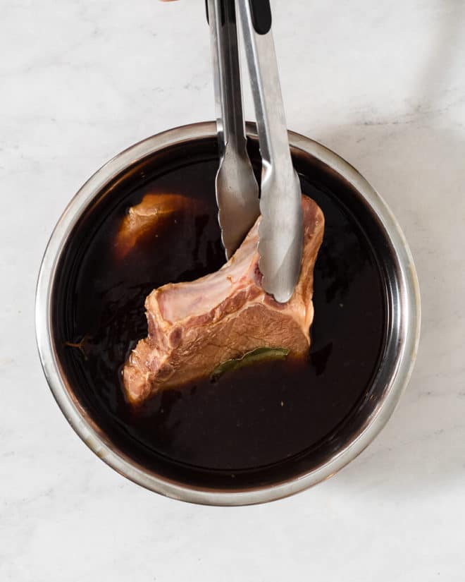 someone pulling a fully brined pork chop out of a large bowl of pork chop brine