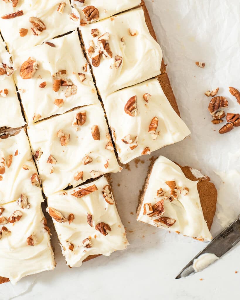 a frosted spice cake topped with pecans sliced into 12 servings on a piece of parchment paper