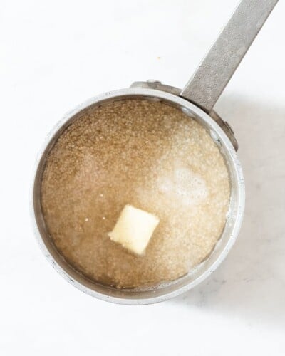 a stainless steel pot of dry white quinoa, water, and butter