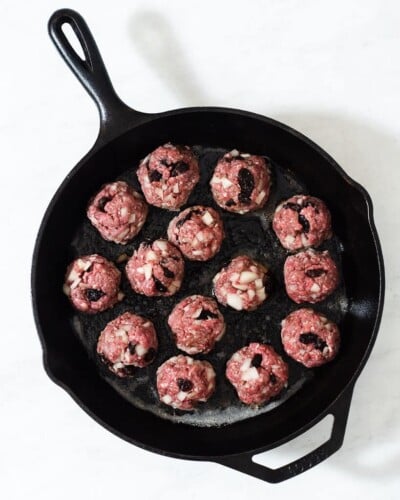 raw greek style meatballs in a cast iron skillet