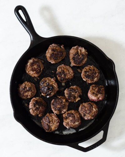 a cast iron skillet with greek style meatballs searing in it