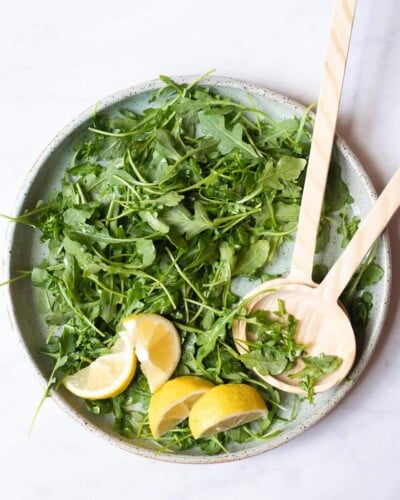 a simple arugula salad on a plate with lemon wedges and wooden serving spoons
