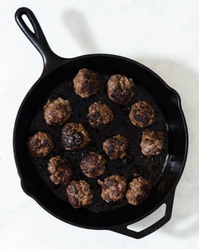 a cast iron skillet with greek style meatballs searing in it