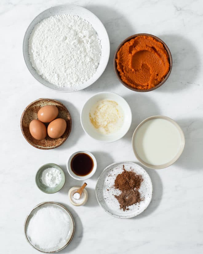 the ingredients for pumpkin pancakes in small bowls and plates on a marble surface