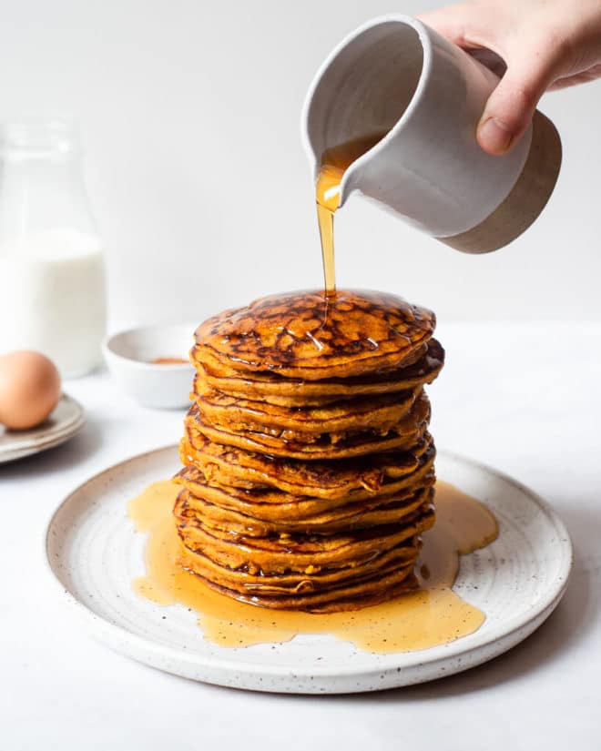 a stack of pumpkin pancakes topped being drizzled with maple syrup
