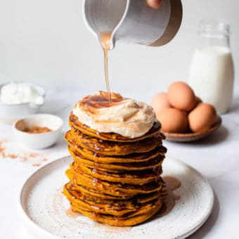 a stack of pumpkin pancakes topped with whipped cream, cinnamon, and maple syrup